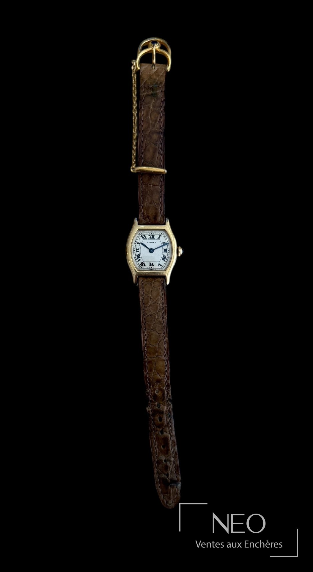 Montre Cartier Tortue de biais sur bracelet cuir brun, avec boucle et chainette visibles.